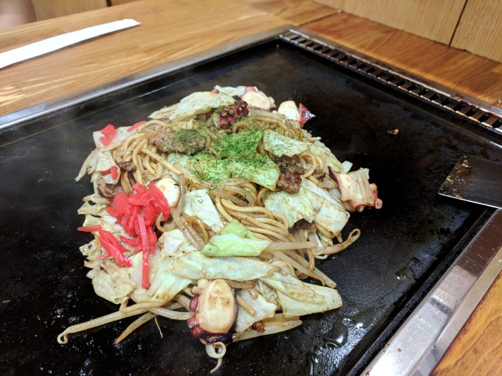 Osaka, Japan Foodie Travelogue - Okaru restaurant serving Okonomiyaki and Yakisoba. Booth seat in the restaurant, with grill at table. Seen here is the Yakisoba, freshly made, with octopus, cabbage and pork.